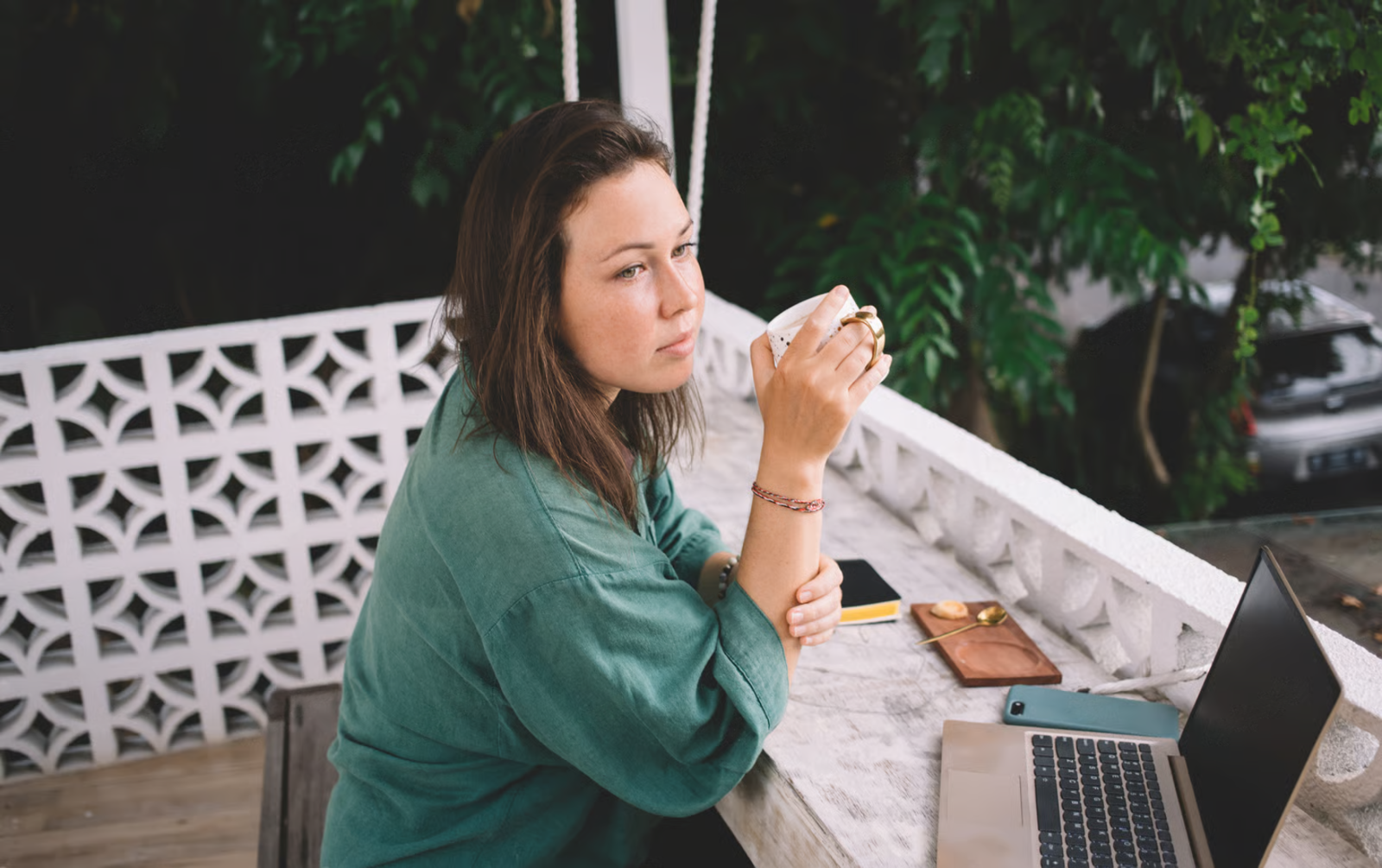 Woman thinking over coffee and laptop outdoors